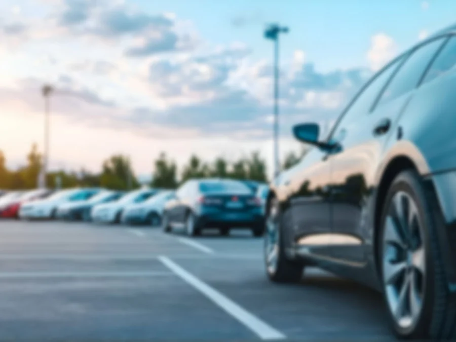 Parkplatz mit mehreren geparkten Autos bei Sonnenuntergang, im Vordergrund ein dunkler Pkw