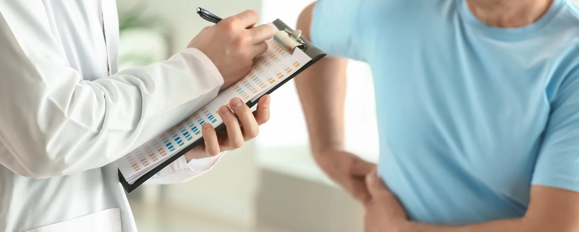 Arzt spricht mit einem Patienten, der sich mit schmerzverzerrtem Gesicht an die Seite fasst.