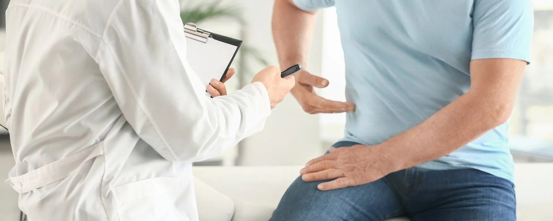 Arzt untersucht einen Patienten mit Rückenschmerzen, der auf der Liege sitzt und auf seine Seite zeigt.