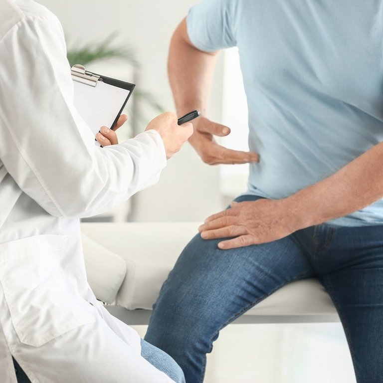 Arzt untersucht einen Patienten mit Rückenschmerzen, der auf der Liege sitzt und auf seine Seite zeigt.
