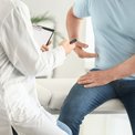 Arzt untersucht einen Patienten mit Rückenschmerzen, der auf der Liege sitzt und auf seine Seite zeigt.