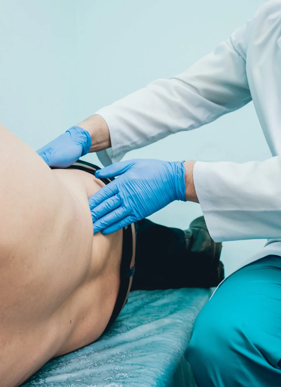 Arzt tastet mit Handschuhen den Rücken eines Patienten während einer Untersuchung ab