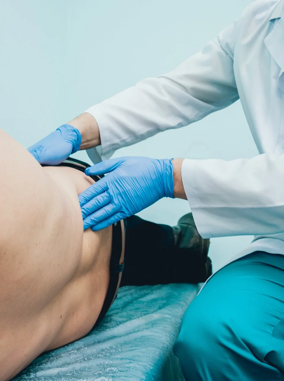 Arzt tastet mit Handschuhen den Rücken eines Patienten während einer Untersuchung ab
