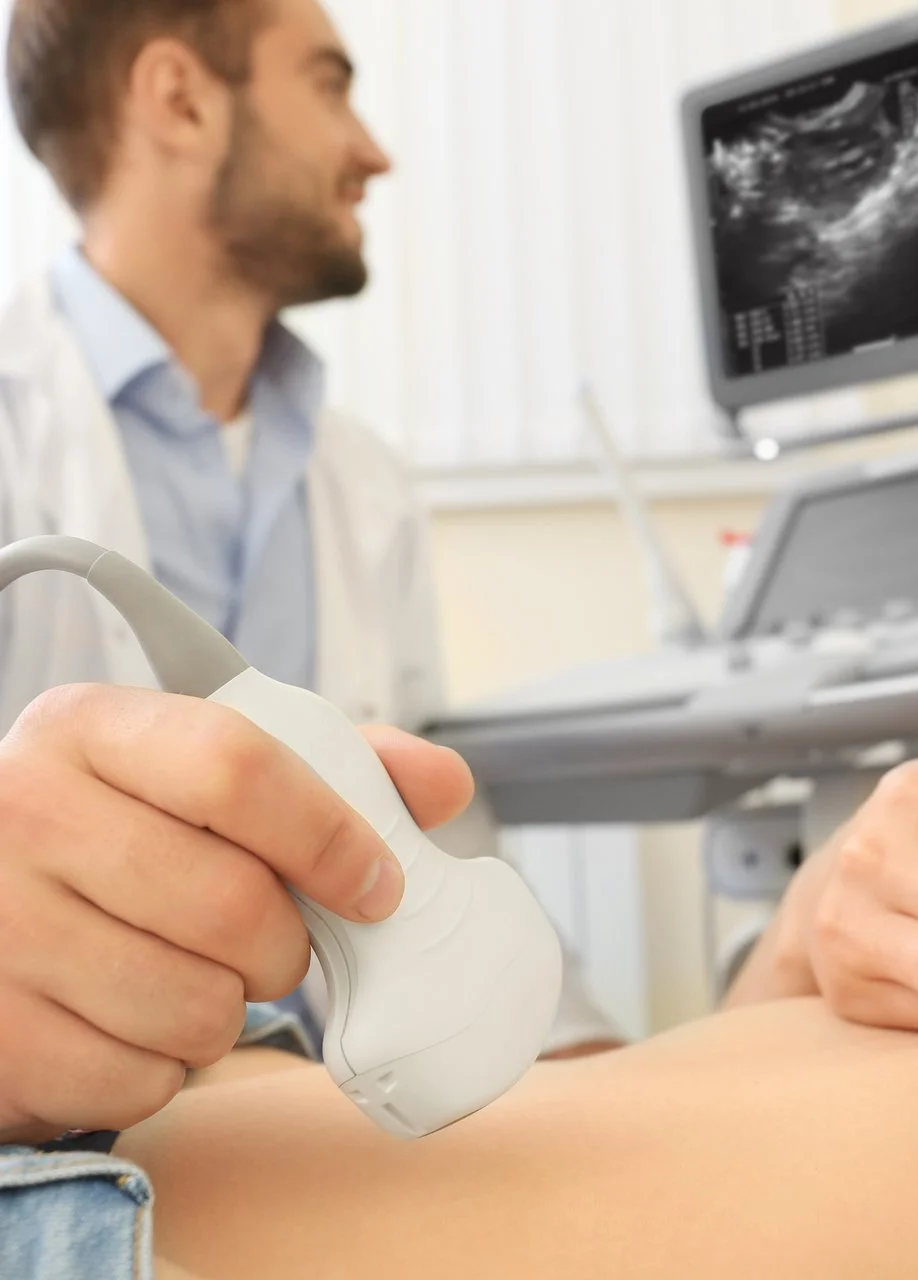 Arzt führt eine Ultraschalluntersuchung am Bauch eines Patienten durch, Monitor zeigt Bildgebung