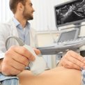 Arzt führt eine Ultraschalluntersuchung am Bauch eines Patienten durch, Monitor zeigt Bildgebung
