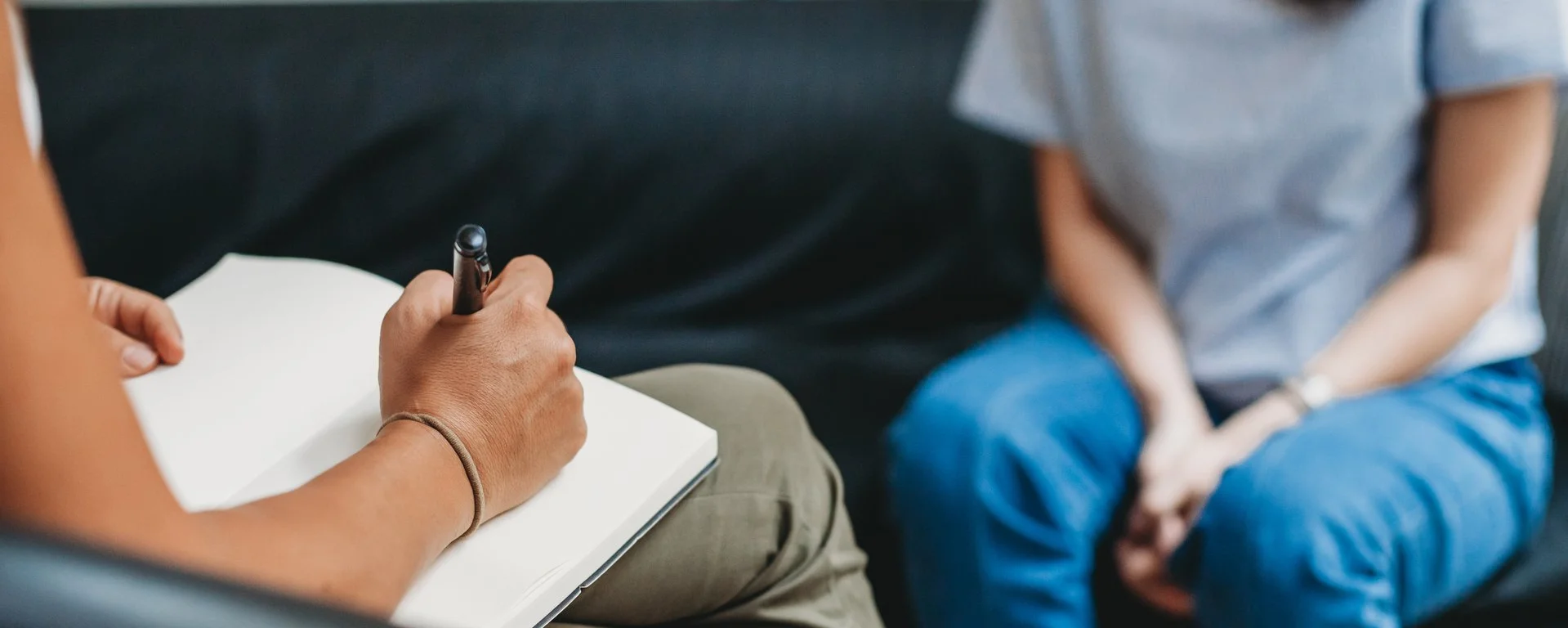 Psychologisches Gespräch: Eine Frau sitzt auf einem Sofa, die Therapeutin macht sich Notizen