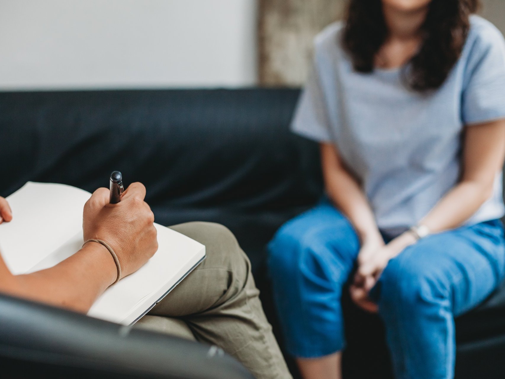 Psychologisches Gespräch: Eine Frau sitzt auf einem Sofa, die Therapeutin macht sich Notizen